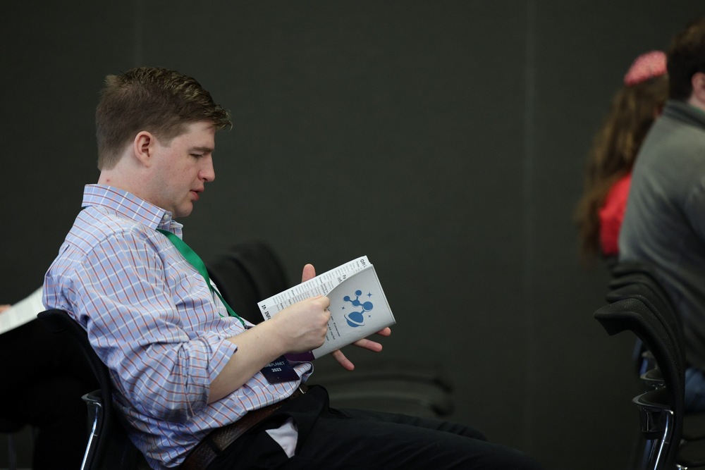 A photograph of Nik Nyby sitting and reading a booklet, while waiting to present his talk.